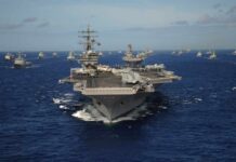 An aircraft carrier surrounded by various naval ships in the ocean