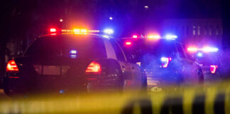 Police cars with flashing lights at a nighttime scene behind crime scene tape