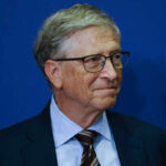 A business leader with glasses smiling in front of a blue background