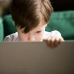 Young boy intently focused on a laptop in a cozy setting