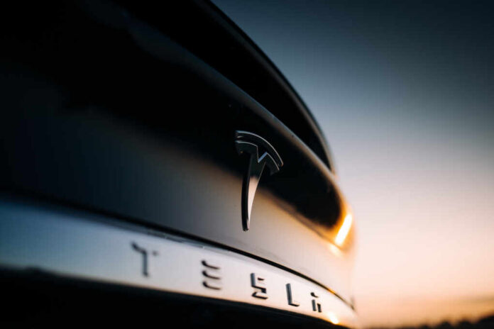 Riga,,Lv,-,Aug,27,,2019:,Tesla,Logo,At,The Close-up of a Tesla logo on a black car with a sunset in the background