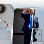 A political figure waving from the steps of an aircraft