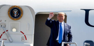 A political figure waving from the steps of an aircraft