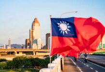 China Tests Taiwan’s Red Line Taiwan flag waving in front of a city skyline during sunset