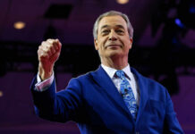 A man in a blue suit raising his fist confidently on stage