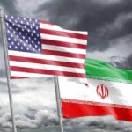 Flags of the United States and Iran waving against a cloudy sky