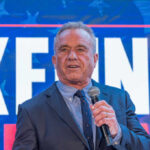 Man in a suit speaking into a microphone at a political event