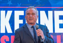 Man in a suit speaking into a microphone at a political event