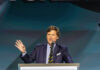 A man in a suit speaking at a podium with a microphone