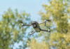 A drone flying against a backdrop of green trees and a blue sky