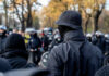 A crowd of masked individuals facing law enforcement in an autumn setting