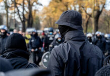 Rubio’s Terror Pivot Sparks Data Uproar A crowd of masked individuals facing law enforcement in an autumn setting