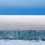 Iceberg Impacts Trigger Antarctic Alarms Ice cliff along a polar glacier under a blue sky