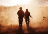 Two soldiers walking through a smoky field at sunset