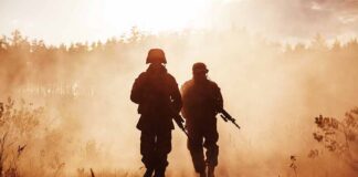 Two soldiers walking through a smoky field at sunset