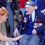 Elderly veteran in wheelchair greeted by woman