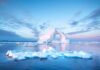 Iceberg with arch formation in calm Arctic sea at sunset