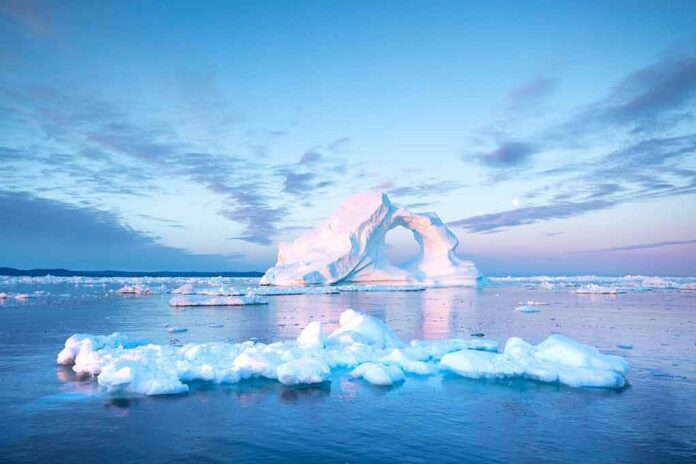 Iceberg with arch formation in calm Arctic sea at sunset