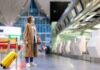 Brain Drain Panic: Why France Bleeds Talent Traveler in mask with yellow suitcase at airport check-in area