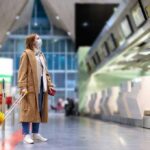 Traveler in mask with yellow suitcase at airport check-in area