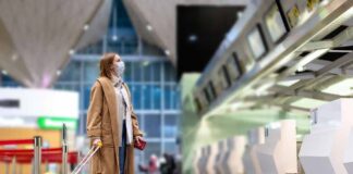 Traveler in mask with yellow suitcase at airport check-in area
