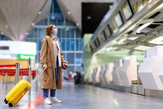 shutterstock_1681005856 Traveler in mask with yellow suitcase at airport check-in area
