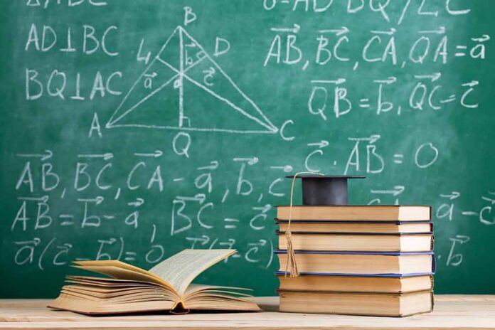 Stack of books with graduation cap in front of chalkboard with math formulas