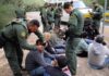 Law enforcement officers process a seated group outdoors