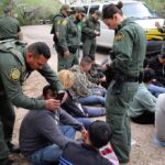 Border Twist: Trespass Charges Explode Law enforcement officers process a seated group outdoors