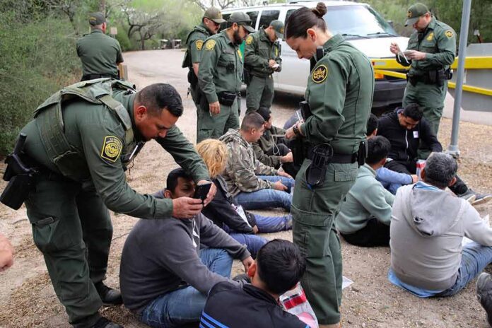 Law enforcement officers process a seated group outdoors
