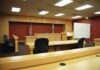 Trump Course Arrest Triggers Court Detour Interior view of an empty courtroom with wooden furniture and American flags