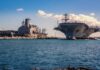 Aircraft carrier and support ships docked at a naval harbor