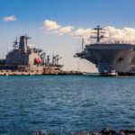 Aircraft carrier and support ships docked at a naval harbor
