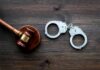 Judge's gavel and metal handcuffs on wooden table