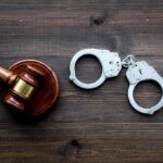 Judge's gavel and metal handcuffs on wooden table