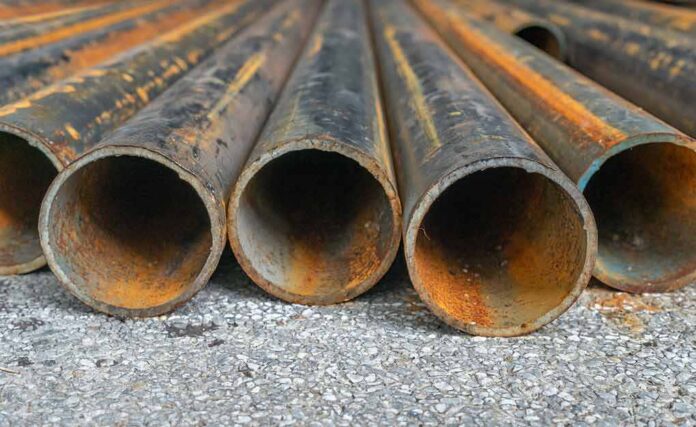 shutterstock_1243306132 Rusty metal pipes laid on gravel