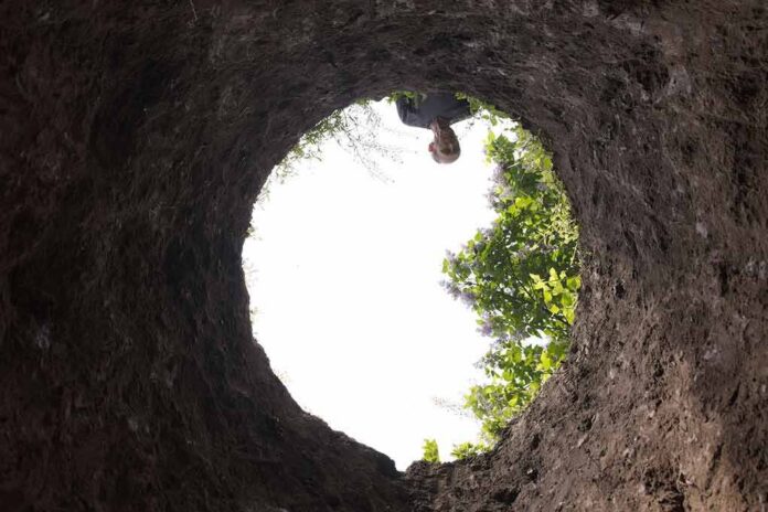 shutterstock_1399622537 Person peering down into a deep dirt hole
