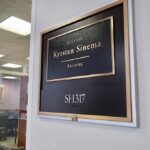 Office door plaque with gold trim outside a glass-walled conference room