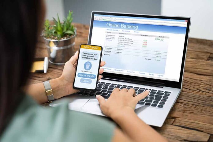 Person using smartphone to approve bank transfer beside laptop with online banking