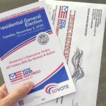 Hand holding election pamphlet and mail-in ballot envelopes