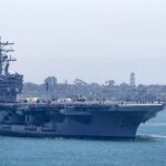 Aircraft carrier escorted by a tugboat in a harbor