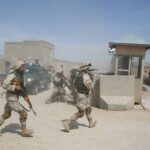 Soldiers in desert uniforms run past a checkpoint amid dust