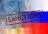 Sanctions text over financial chart and flag with coin stacks