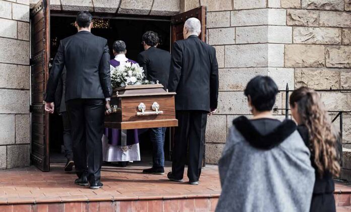 Pallbearers carry a casket into a stone church
