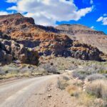 Dirt road winding through rocky desert hills under a bright blue sky