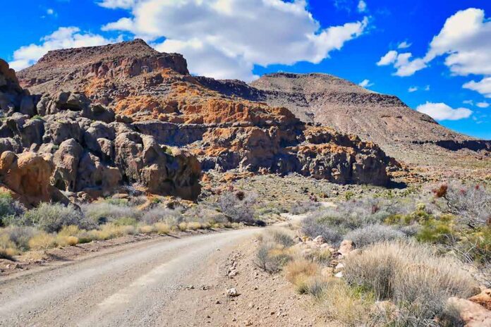 shutterstock_2300397105 Dirt road winding through rocky desert hills under a bright blue sky