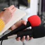 Hollywood Star Drops Patriotism Bomb Journalist holding two microphones while writing in a notebook
