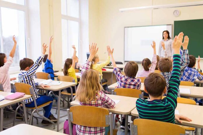 Students raise hands in a classroom while a teacher stands at the front