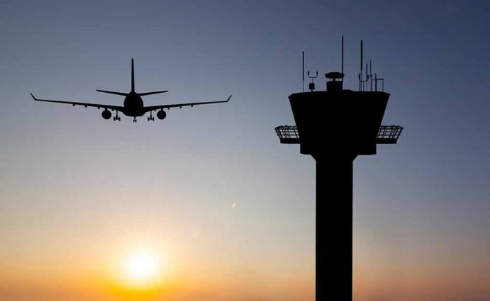 Airplane approaching runway near airport control tower at sunset