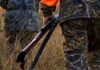 Hunter in camouflage holding a rifle in tall grass